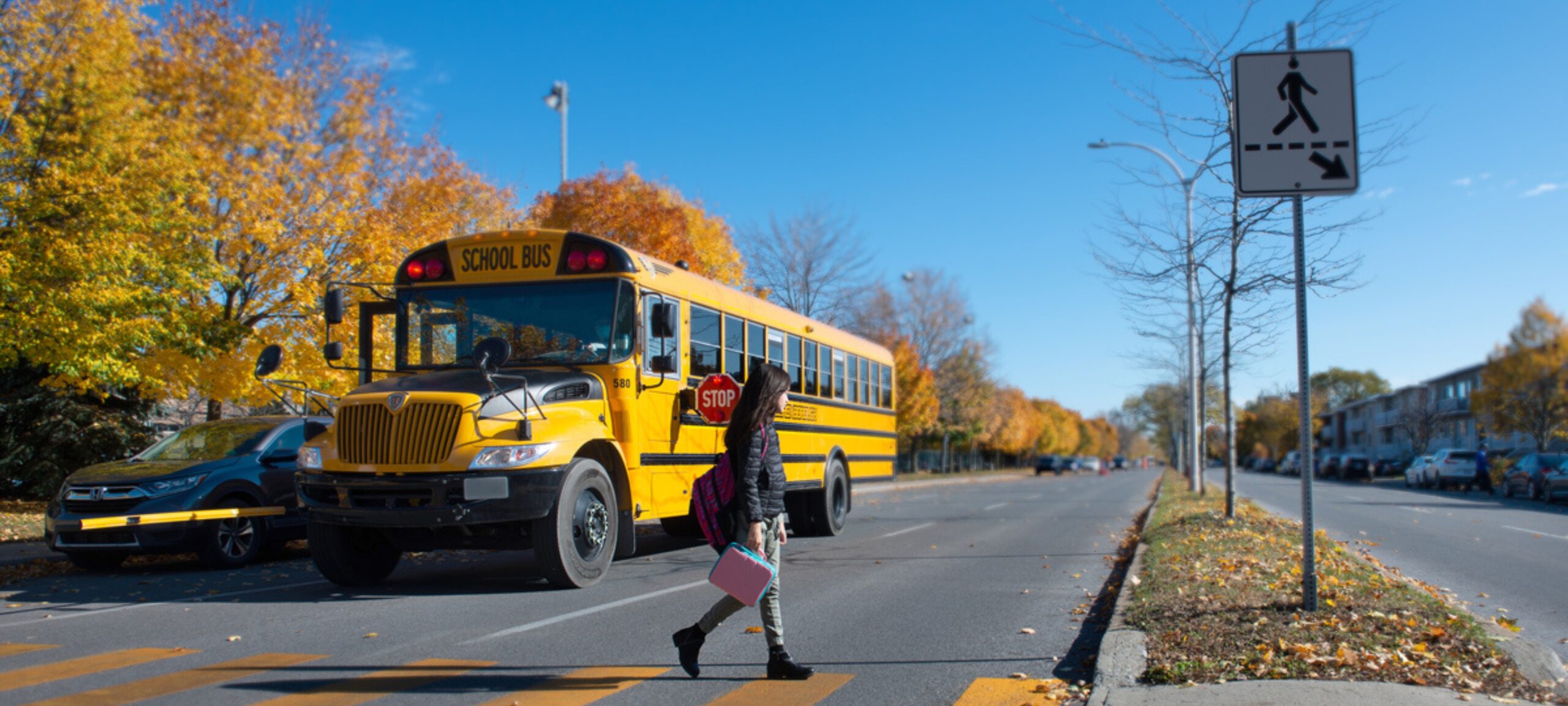 Child crossing the street in front of a school bus with its stop-arm extended